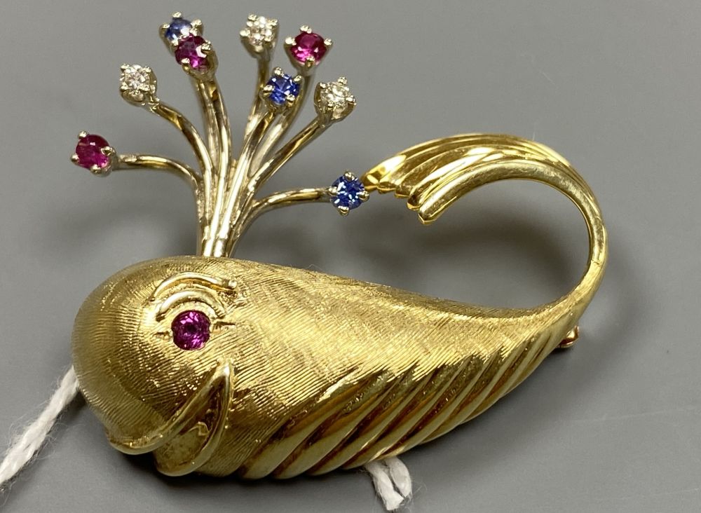A novelty continental yellow metal (engraved 14k), ruby diamond and sapphire set happy whale brooch,